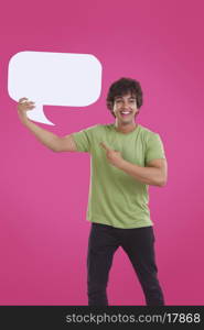 Smiling young man pointing at speech bubble over pink background