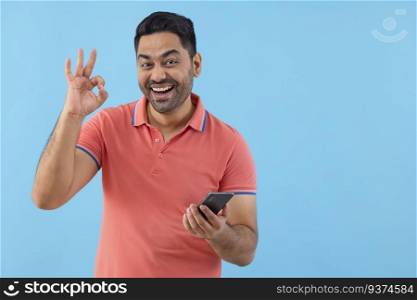 Smiling young man showing OK sign while using Smartphone