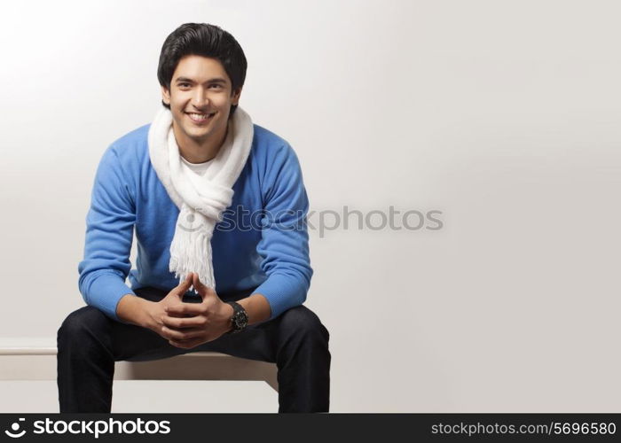 Smiling young man sitting over colored background