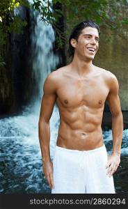 Smiling young man standing by waterfall, front view