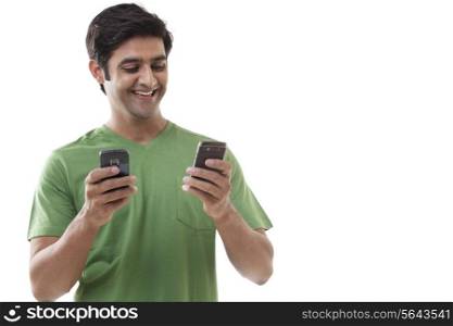 Smiling young man text messaging through cell phones