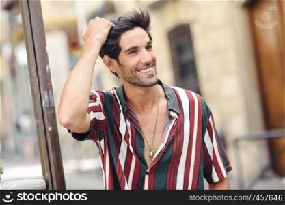 Smiling young man touching his hair wearing casual clothes in urban background.. Smiling young man touching his hair wearing casual clothes outdoors