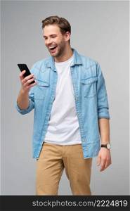 Smiling young man wearing jeans shirt taking selfie photo on smartphone or making video call standing over grey studio background.. Smiling young man wearing jeans shirt taking selfie photo on smartphone or making video call standing over grey studio background