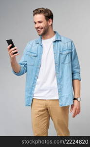 Smiling young man wearing jeans shirt taking selfie photo on smartphone or making video call standing over grey studio background.. Smiling young man wearing jeans shirt taking selfie photo on smartphone or making video call standing over grey studio background