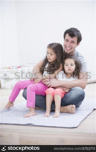 Smiling young man with daughters sitting in his lap at home