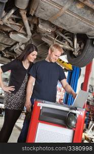 Smiling young mechanic standing with customer and looking at laptop