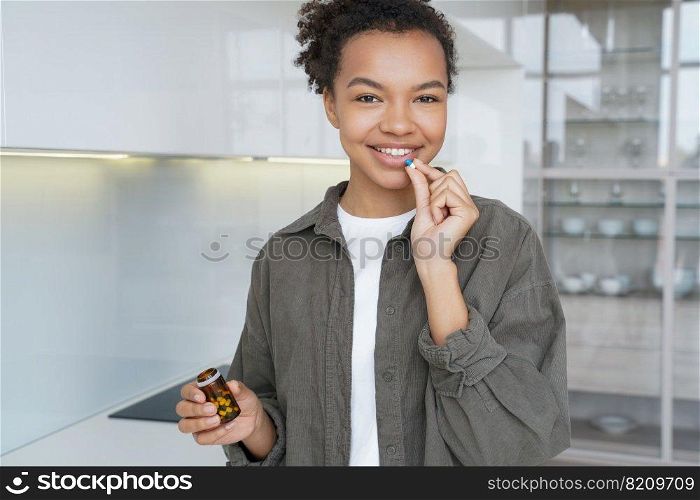 Smiling young mixed race girl holding pills for female skin health, standing at home, looking at camera. Happy biracial lady taking vitamins, dietary supplement. Healthy lifestyle, skincare concept.. Smiling young biracial girl holds pills, taking vitamins, dietary supplement for healthy skin, hairs