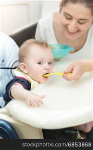 Smiling young mother feeding her baby in highchair
