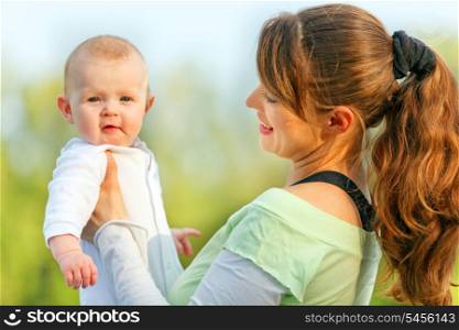Smiling young mother holding surprised baby in hands at summer day&#xA;