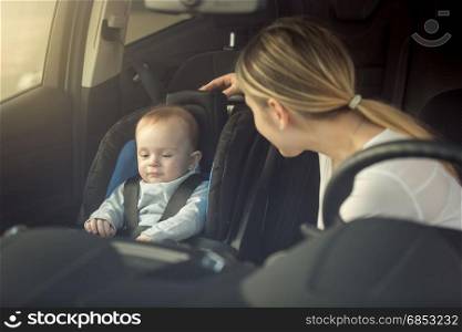 Smiling young mother looking at her child sitting in safety seat