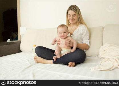 Smiling young mother sitting on bed with her baby boy