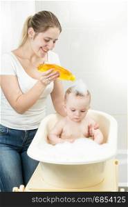 Smiling young mother washing her baby&rsquo;s head with shampoo