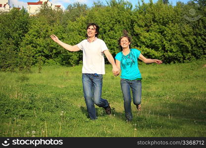 smiling young pair runs, keeping for hands, on grass in park