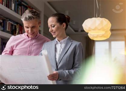 Smiling young saleswoman and male client looking at floor plan in apartment