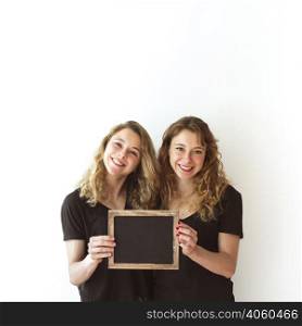 smiling young sister together holding blank slate isolated white backdrop