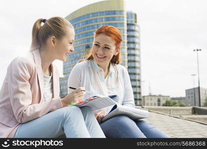 Smiling young university students studying against building