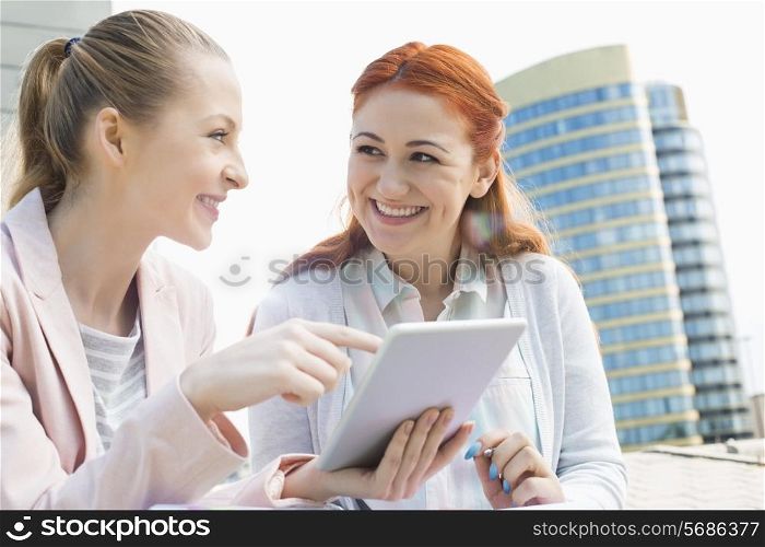 Smiling young university students using tablet PC against building