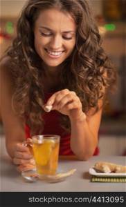 Smiling young woman adding cane sugar cube in ginger tea