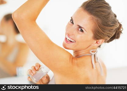 Smiling young woman applying roller deodorant on underarm in bathroom