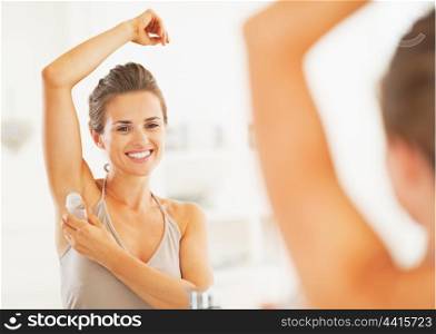 Smiling young woman applying roller deodorant on underarm in bathroom
