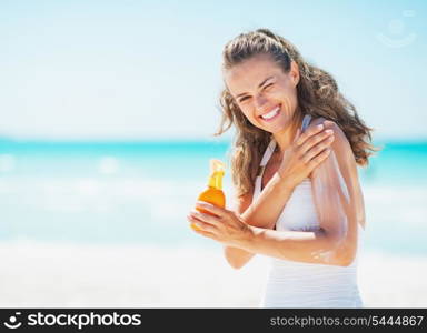 Smiling young woman applying sun block creme on beach