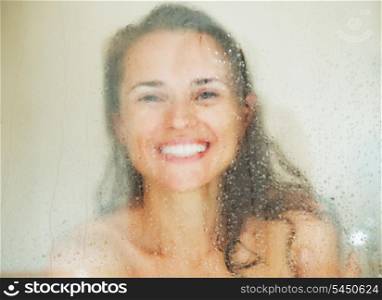 Smiling young woman behind weeping glass shower door