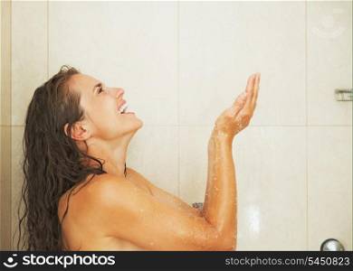 Smiling young woman catching water drops in shower