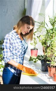 smiling young woman cleaning surface near potted plant sunlight