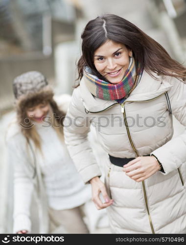 Smiling young woman climbing stairs with friend outdoors