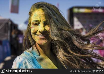 smiling young woman covered her face with holi color looking camera