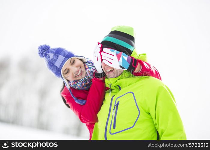 Smiling young woman covering man&rsquo;s eyes in winter