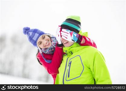 Smiling young woman covering man&rsquo;s eyes in winter