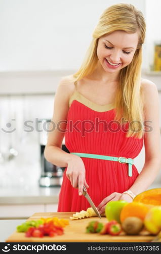 Smiling young woman cutting fresh fruits salad