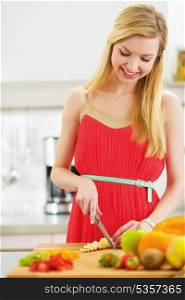 Smiling young woman cutting fresh fruits salad