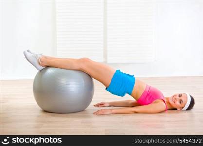 Smiling young woman doing abdominal crunch on fitness ball at living room&#xA;