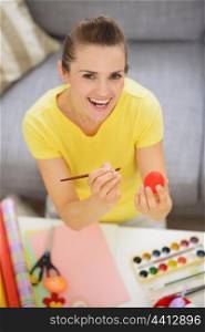 Smiling young woman drawing on Easter red egg