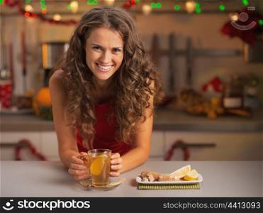 Smiling young woman drinking ginger tea in christmas decorated kitchen