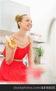Smiling young woman eating banana in kitchen