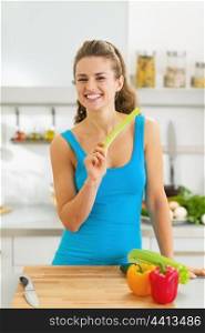 Smiling young woman eating celery in modern kitchen
