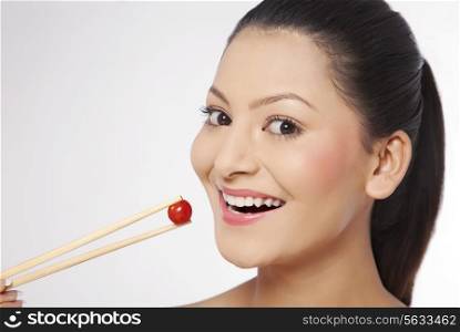 Smiling young woman eating cherry tomato with chop sticks