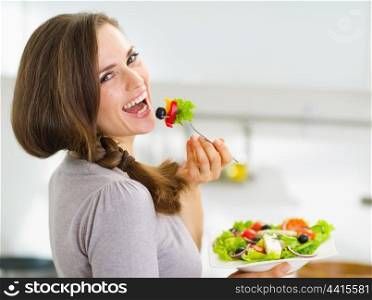 Smiling young woman eating fresh salad in modern kitchen