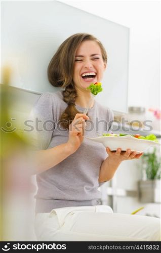 Smiling young woman eating fresh salad in modern kitchen