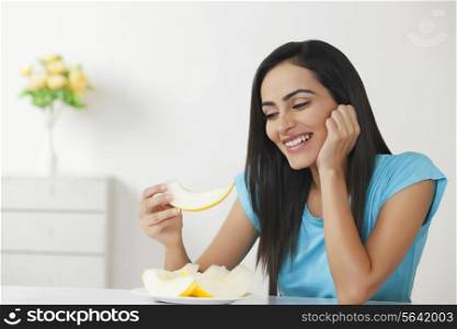 Smiling young woman eating melon at home