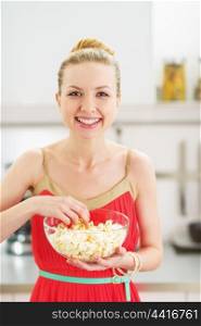 Smiling young woman eating popcorn in kitchen