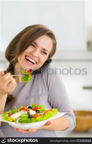 Smiling young woman eating salad and talking mobile phone