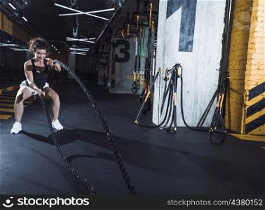 smiling young woman exercising with battle ropes