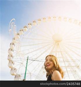 smiling young woman front white giant ferris wheel against blue sky