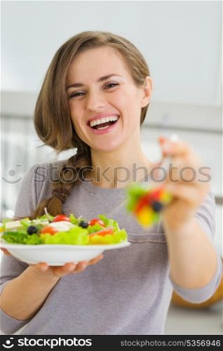 Smiling young woman giving fork with salad