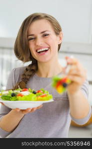 Smiling young woman giving fork with salad