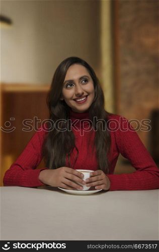Smiling young woman having cup of coffee looking away